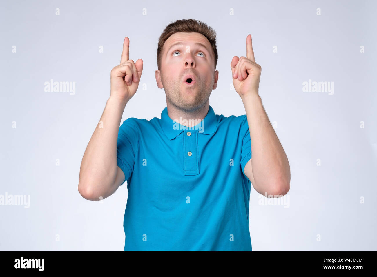 Beau jeune homme en tee-shirt bleu pointant vers le haut avec son doigt Banque D'Images