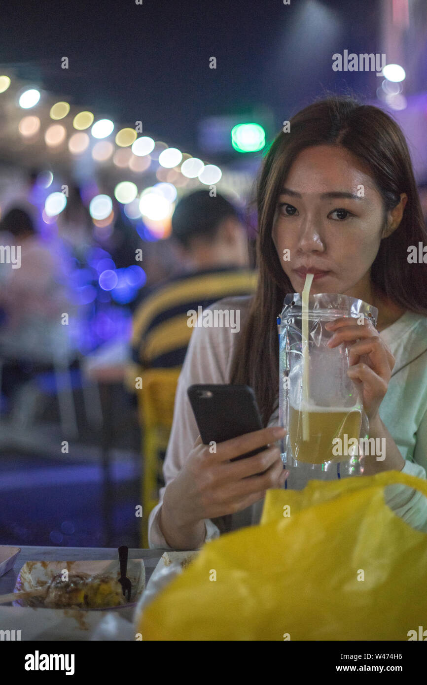 Une femme qui boit de la bière à un marché de nuit. Banque D'Images