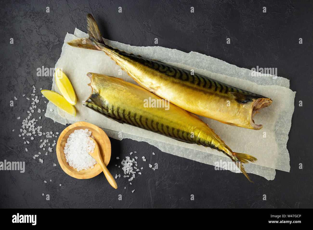 Le poisson fumé ou maquereau Scomber sur un papier parchemin blanc. Fond noir en foncé ou noir. Vue d'en haut. Banque D'Images