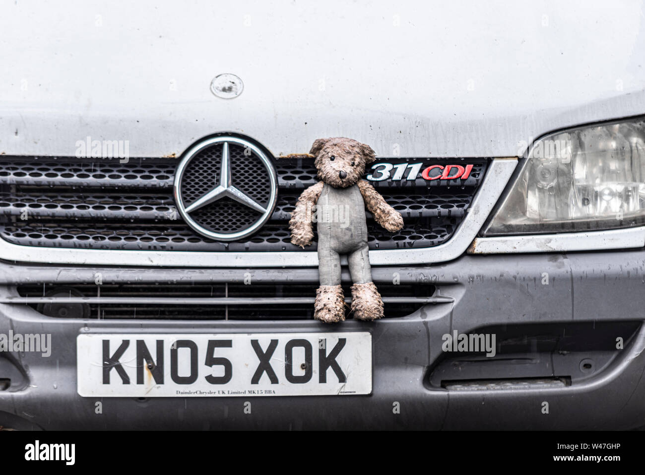 Vieux van avec sad portés à l'enfant surmonté toy ours attaché à la grille capot avant. Humide de pluie et sale de la route. Gaines Banque D'Images