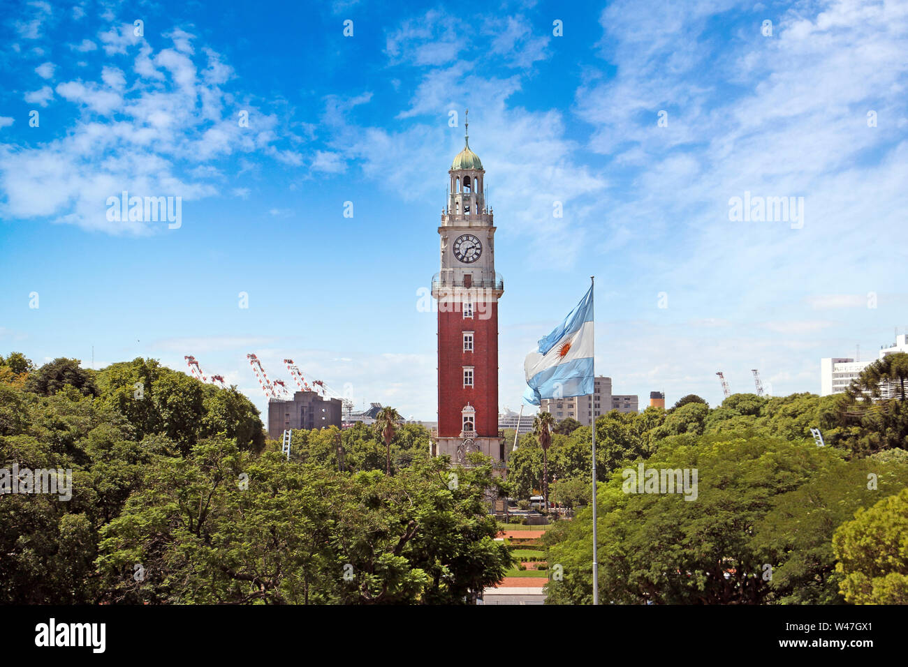Vue sur le drapeau argentin et un tour de l'horloge rouge derrière des arbres, contre un ciel d'été bleu avec quelques nuages blancs. Banque D'Images