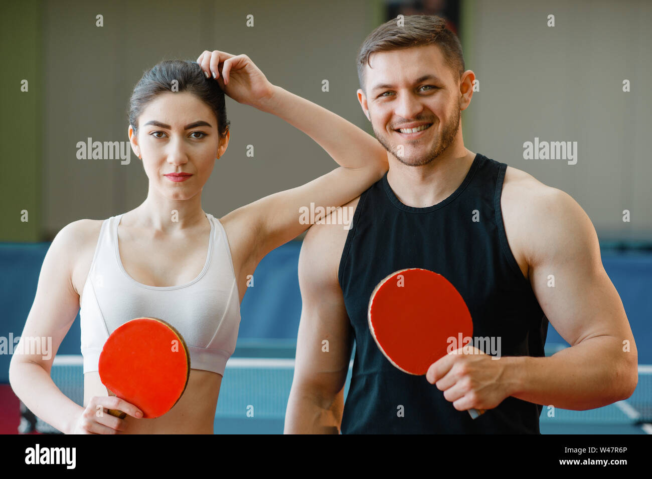 L'homme et la femme est titulaire des raquettes de ping-pong à l'intérieur.  Couple in sportswear joue au tennis de table dans une salle de sport.  Hommes et des femmes dans un club