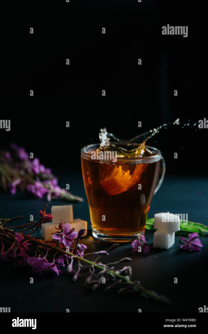 Verre tasse de thé doux chaud noir brun avec bulles et éclaboussures de la pièce de sucre dissolvant projetée et deux morceaux de sucre blanc. Sally floraison Banque D'Images