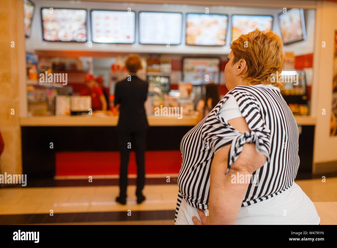 Grosse femme au fast food restaurant menu. L'excès de personne de sexe féminin l'achat, la restauration rapide problème d'obésité Banque D'Images