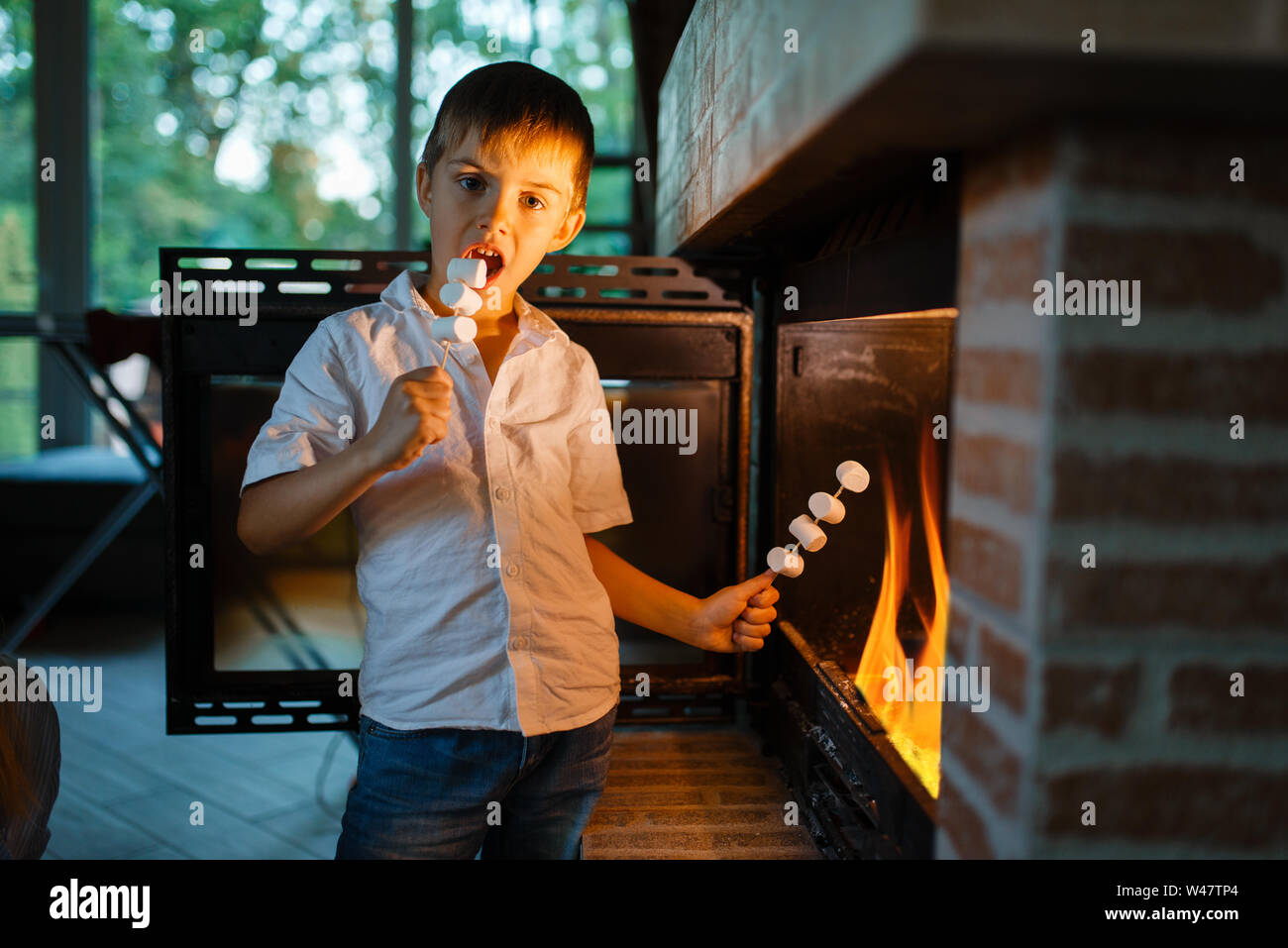 Petit garçon saucisses à frire sur bâton à cheminée dans la chambre. Cuisine enfant la viande grillée sur le feu à la maison, l'enfance heureuse Banque D'Images