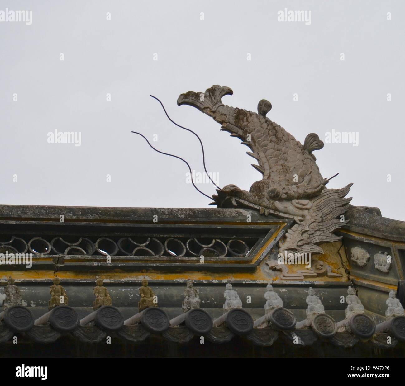 Statue de pierre d'un dragon chinois avec le corps d'un poisson sculpté, de manger le toit d'une construction traditionnelle en Asie, contre un ciel gris Banque D'Images