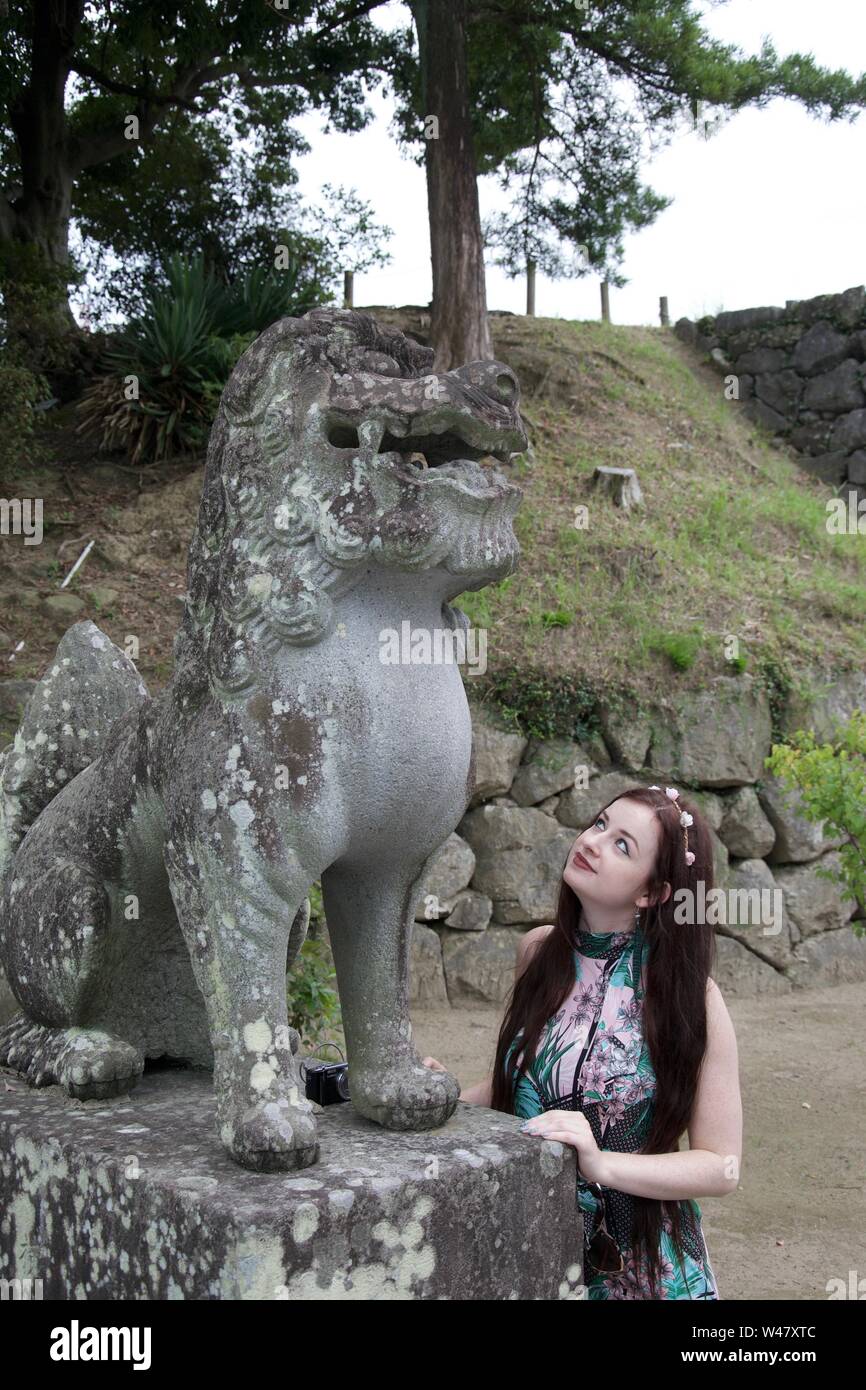 Un quartier à la mode, aux cheveux longs, brune, caucasian girl hippie et admirer un ancien japonais endommagés statue d'un monstre mythique (ou dragon Banque D'Images