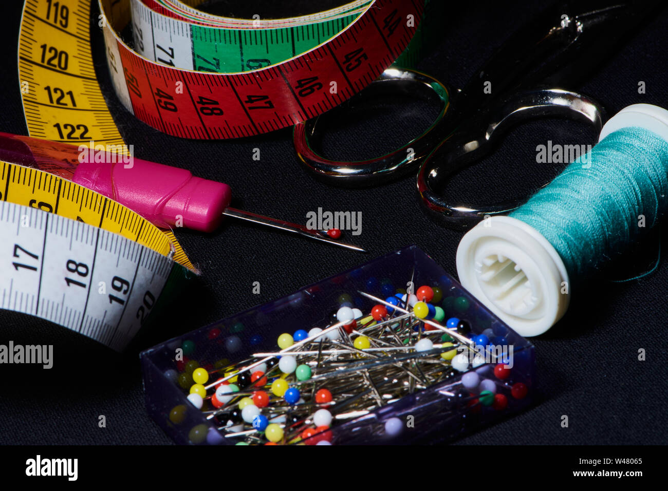 Couleur macro photo de différents outils de couture comme des ciseaux, des épingles, du fil à coudre sur un fond sombre Banque D'Images