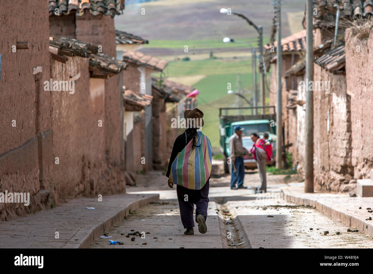 Une dame avec un sac à dos coloré marche dans une rue de la ville de Maras dans la Vallée Sacrée des Incas au Pérou. Banque D'Images