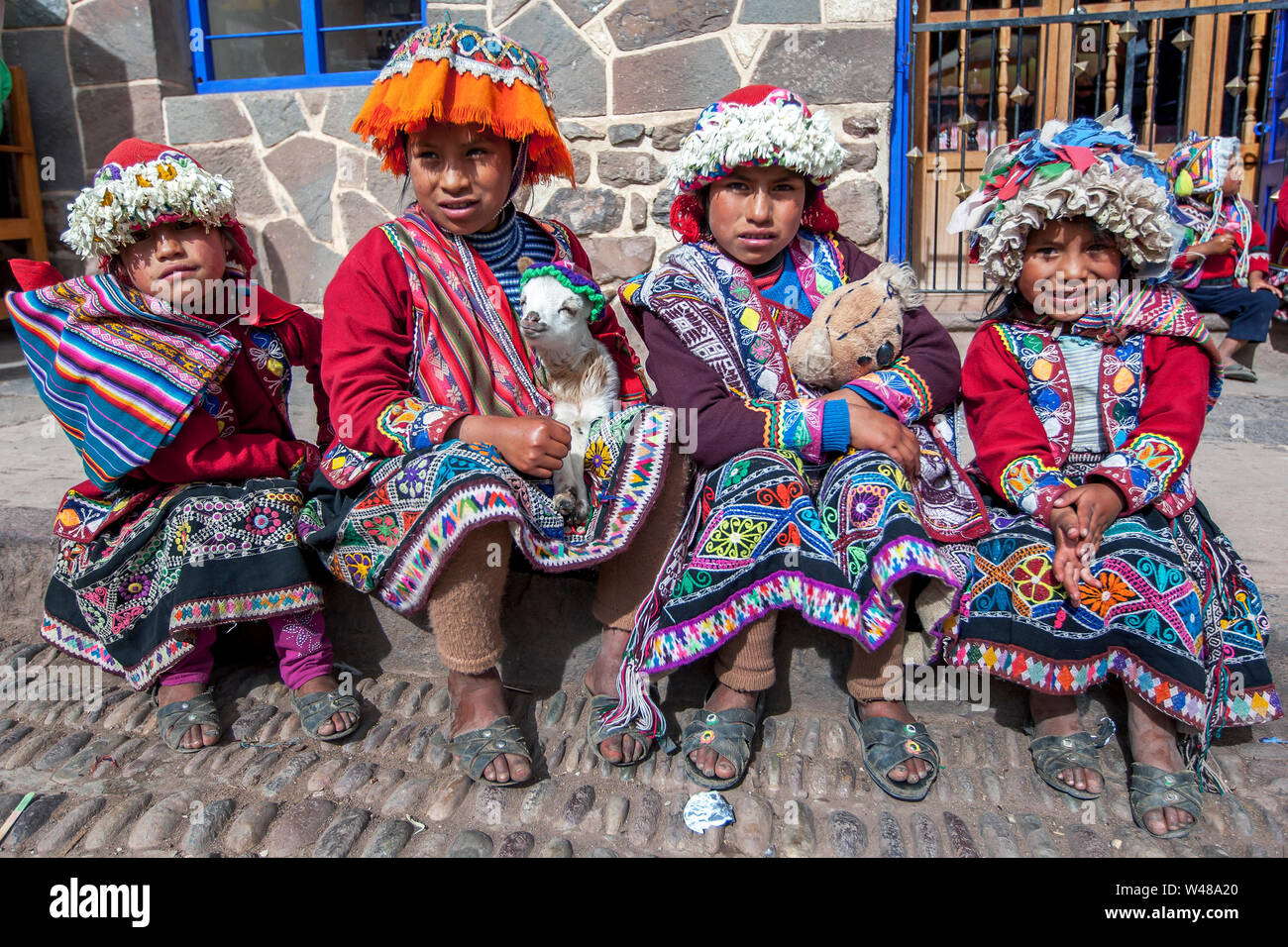 Les jeunes filles habillés en costume traditionnel et tenant un agneau s'asseoir sur une étape au marché de Pisac (Vallée Sacrée des Incas au Pérou). Banque D'Images