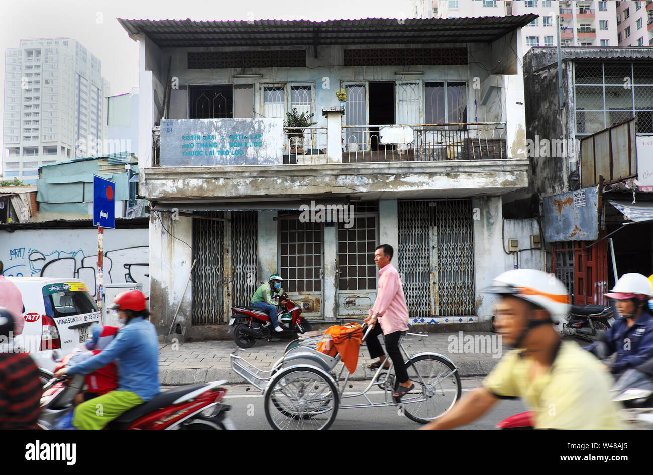 Les gens rouler en moto, pedicab déplacer sur l'ensemble de la rue Vieille maison de deux étages, l'homme d'attendre à l'ancienne façade maison, Vietnam, Ho Chi Minh city Banque D'Images