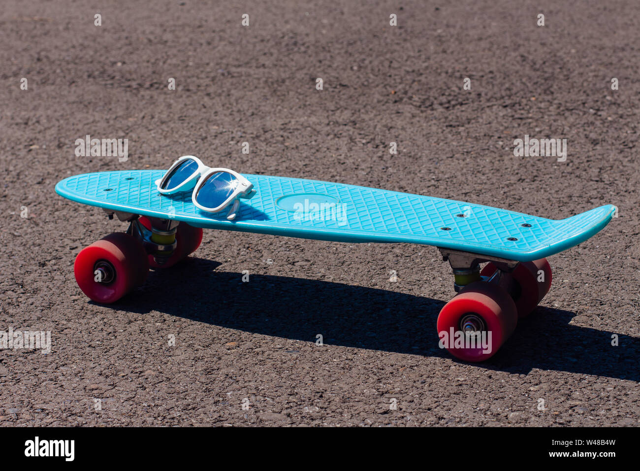 Lunettes de soleil sur une planche à roulettes en plastique bleu avec roues conseil penny rose se dresse sur la piste. Banque D'Images