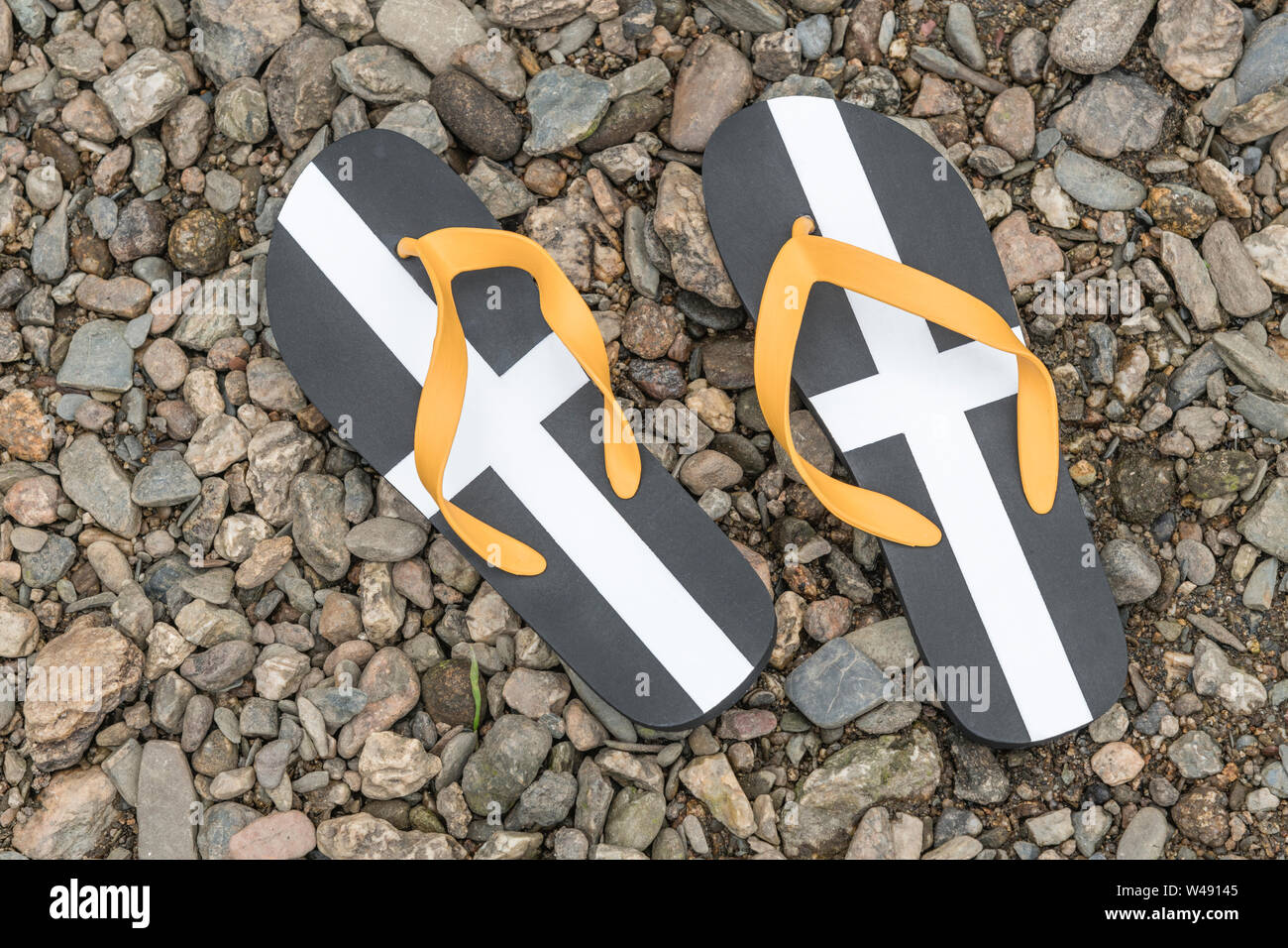 Cornish St Piran's flag tongs sur galets de la rivière. Métaphore UK, vacances vacances vacances chez soi à la maison, Cornwall, Cornwall, maison de vacances Cornish Banque D'Images