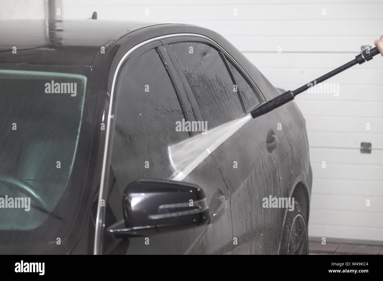 Un travailleur masculin se lave fenêtre d'une voiture noire avec un appareil à haute pression où l'eau et élimine la mousse et les produits chimiques dans un véhicule delin Banque D'Images