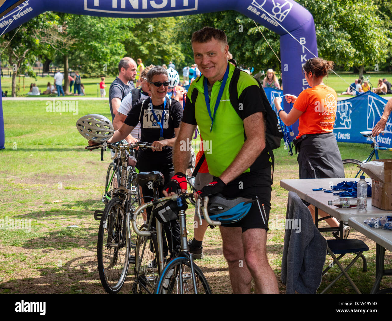 Cambridge, UK. 21, juillet 2019. Un sourire d'un cycliste qui a juste fini de circonscription de Londres à Cambridge. Derrière lui d'autres finishers reçoivent des médailles pour remplir les 60 mile ride. Crédit : Alex Skinner/Alamy live news Banque D'Images