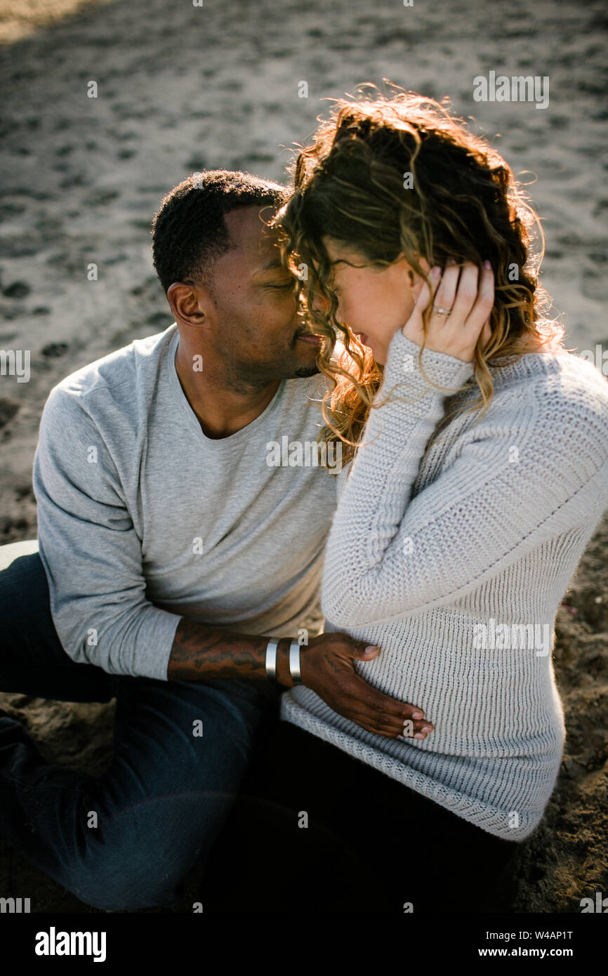 Mari et femme embrasser comme mari touche pregnant belly on beach Banque D'Images