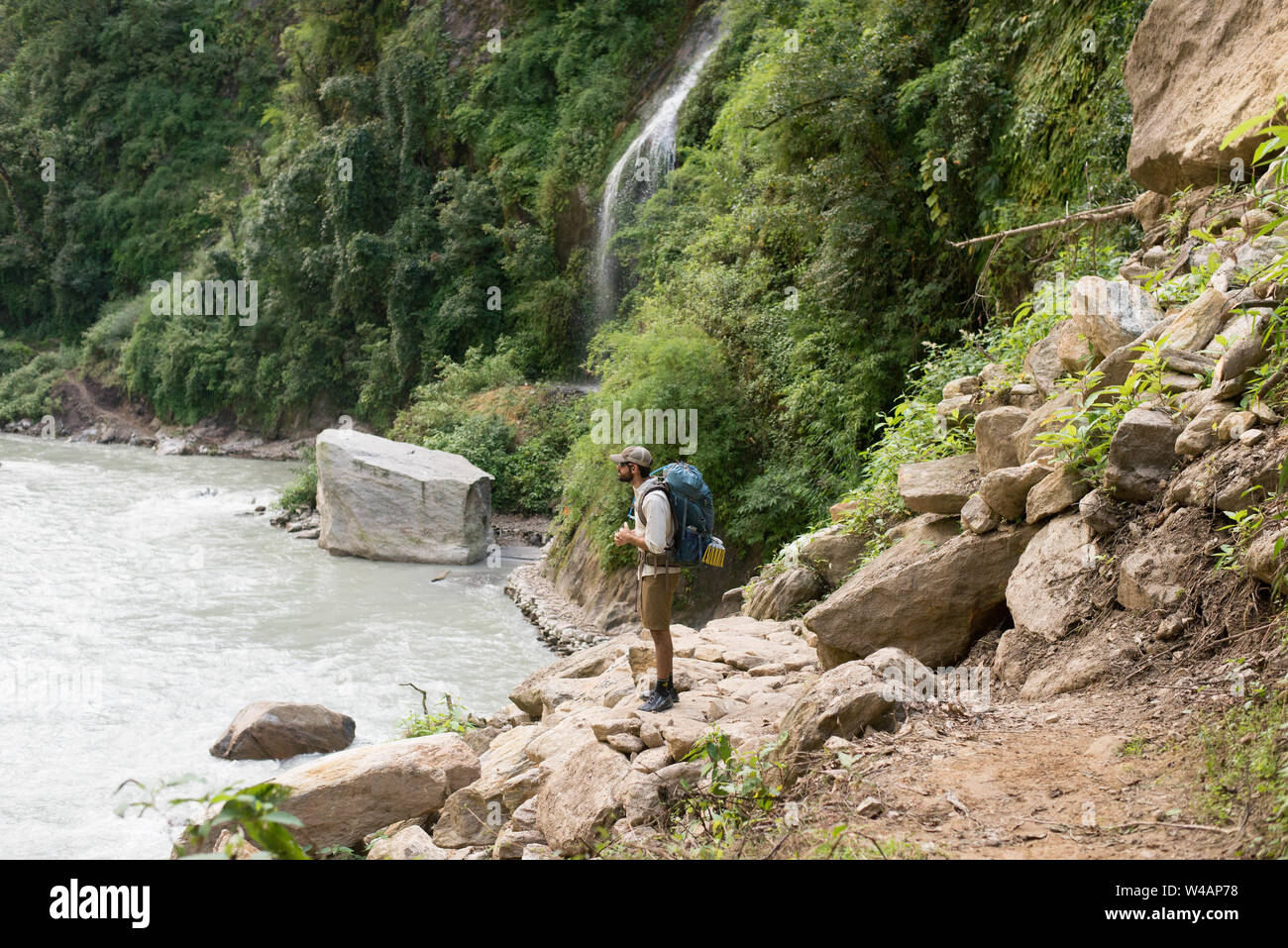 Jeune homme randonnée en montagne le long de la rivière avec cascade Banque D'Images