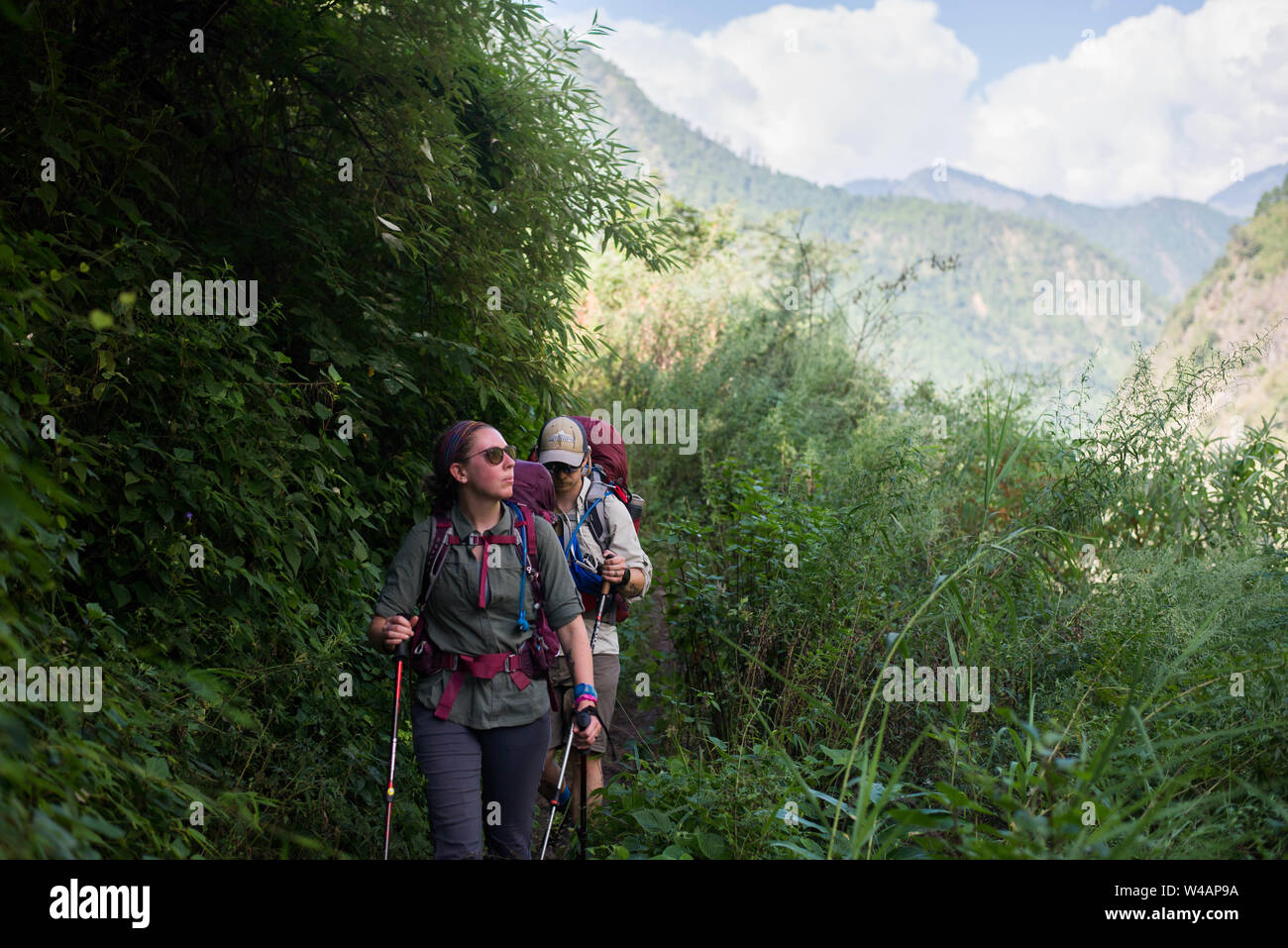 Jeune couple de la randonnée à travers les hautes herbes avec des montagnes Banque D'Images