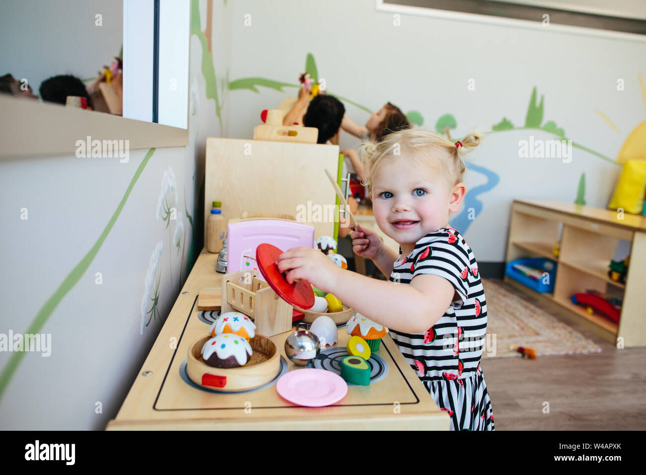 Cute blonde girl smiles at camera comme elle joue avec cuisinière jouet Banque D'Images