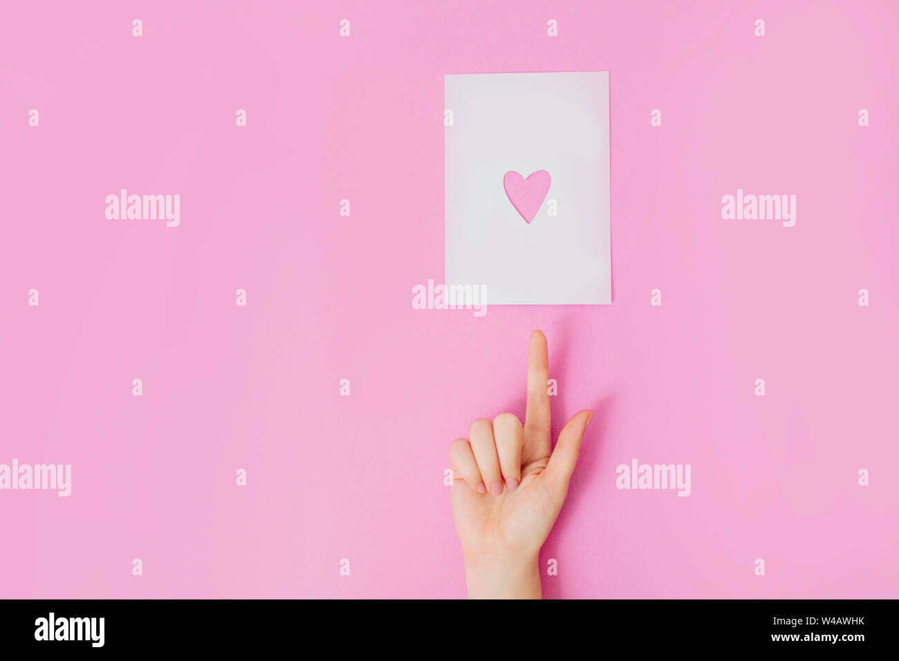 Manucure avec main de femme sur un fond rose pointant sur une feuille de papier blanc en forme de coeur avec des trous. Banque D'Images