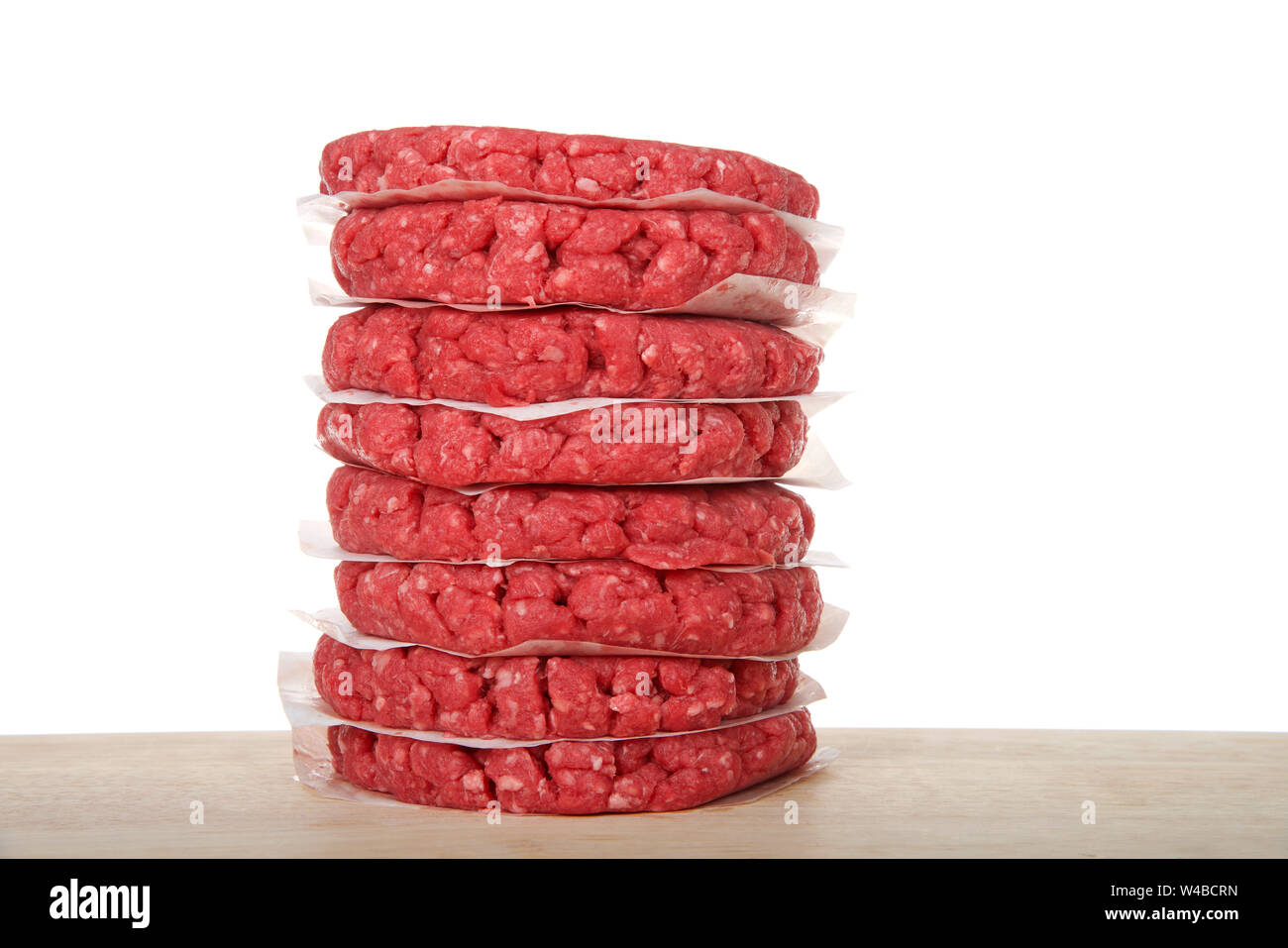 Pile de galettes de viande hachée crue sur une table en bois avec des morceaux de papier sulfurisé entre les burgers pour les empêcher de coller. Isolé sur whit Banque D'Images