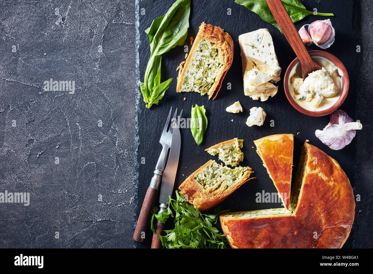 Close-up de haricots verts et épinards Tarte au fromage bleu ardoise noire en tranches sur un plateau avec crème au fromage bleu sauce dans un bol sur une table, la vue à partir de Banque D'Images
