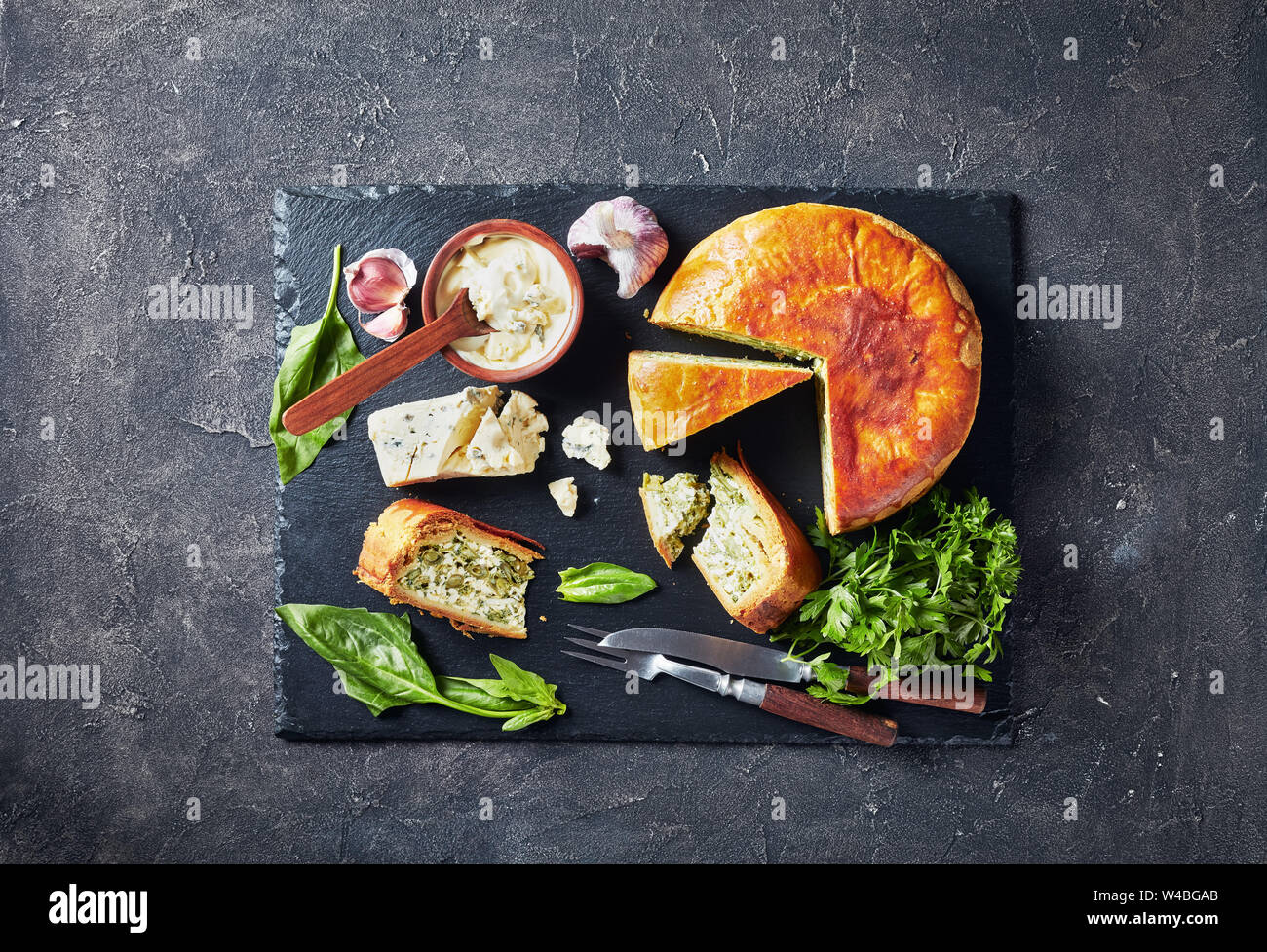 Haricots verts et épinards Tarte au fromage bleu ardoise noire en tranches sur un plateau avec crème au fromage bleu sauce dans un bol sur une table en béton, d'un point de vue horizontal Banque D'Images