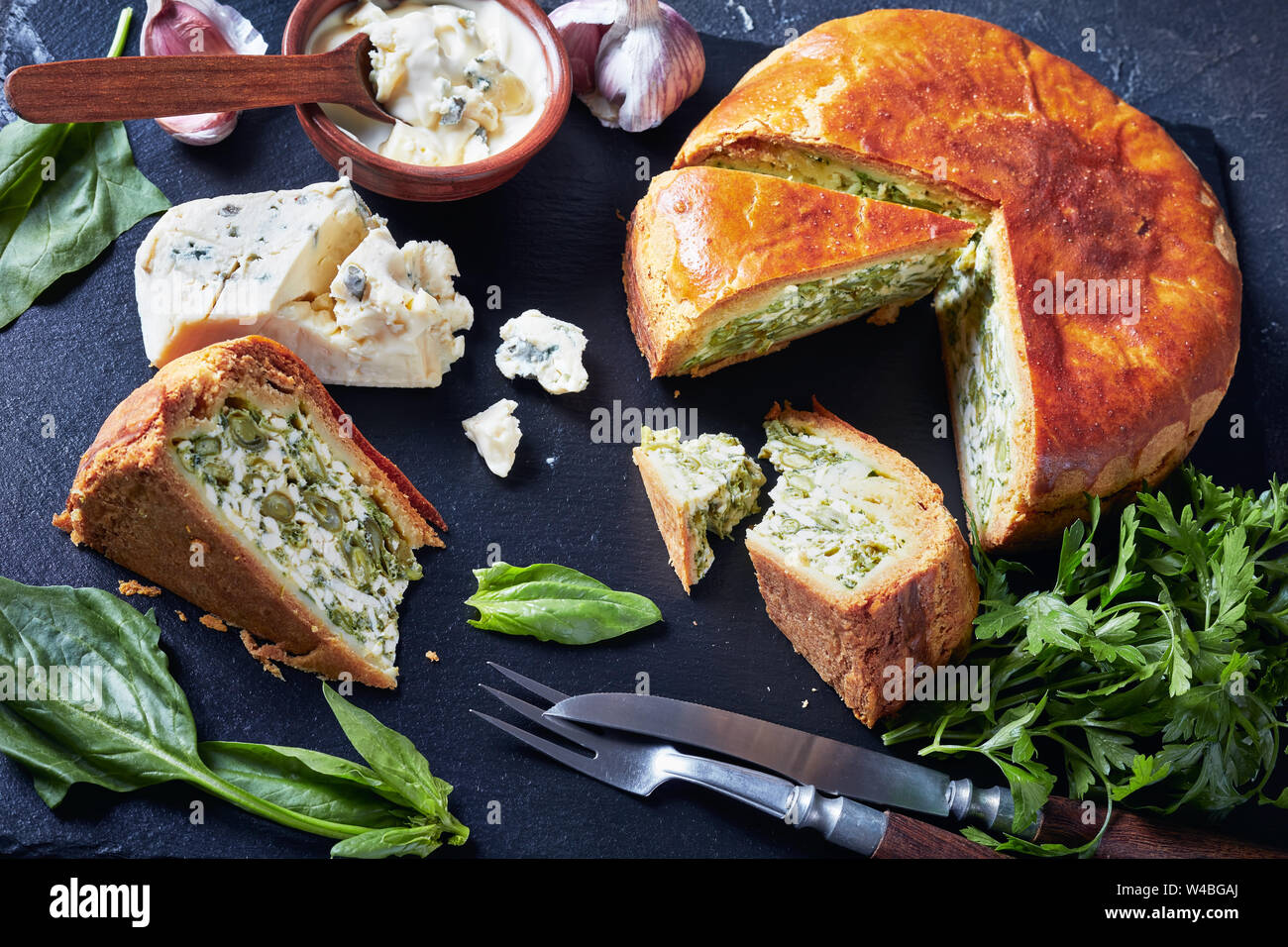 Close-up de haricots verts et épinards Tarte au fromage bleu ardoise noire en tranches sur un plateau avec crème au fromage bleu sauce dans un bol sur une table horizontale, béton Banque D'Images
