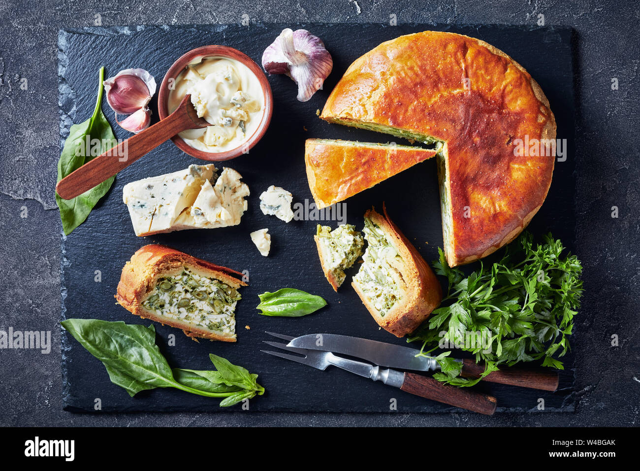 Close-up de haricots verts et épinards Tarte au fromage bleu ardoise noire en tranches sur un plateau avec crème au fromage bleu sauce dans un bol sur une table horizontale, béton Banque D'Images