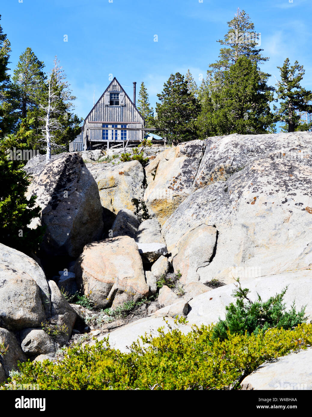 Chalet de montagne en bois patiné gris entouré d'arbres verts et de granit surplombant Caples Lake, la Sierra Nevada, en Californie, USA Banque D'Images