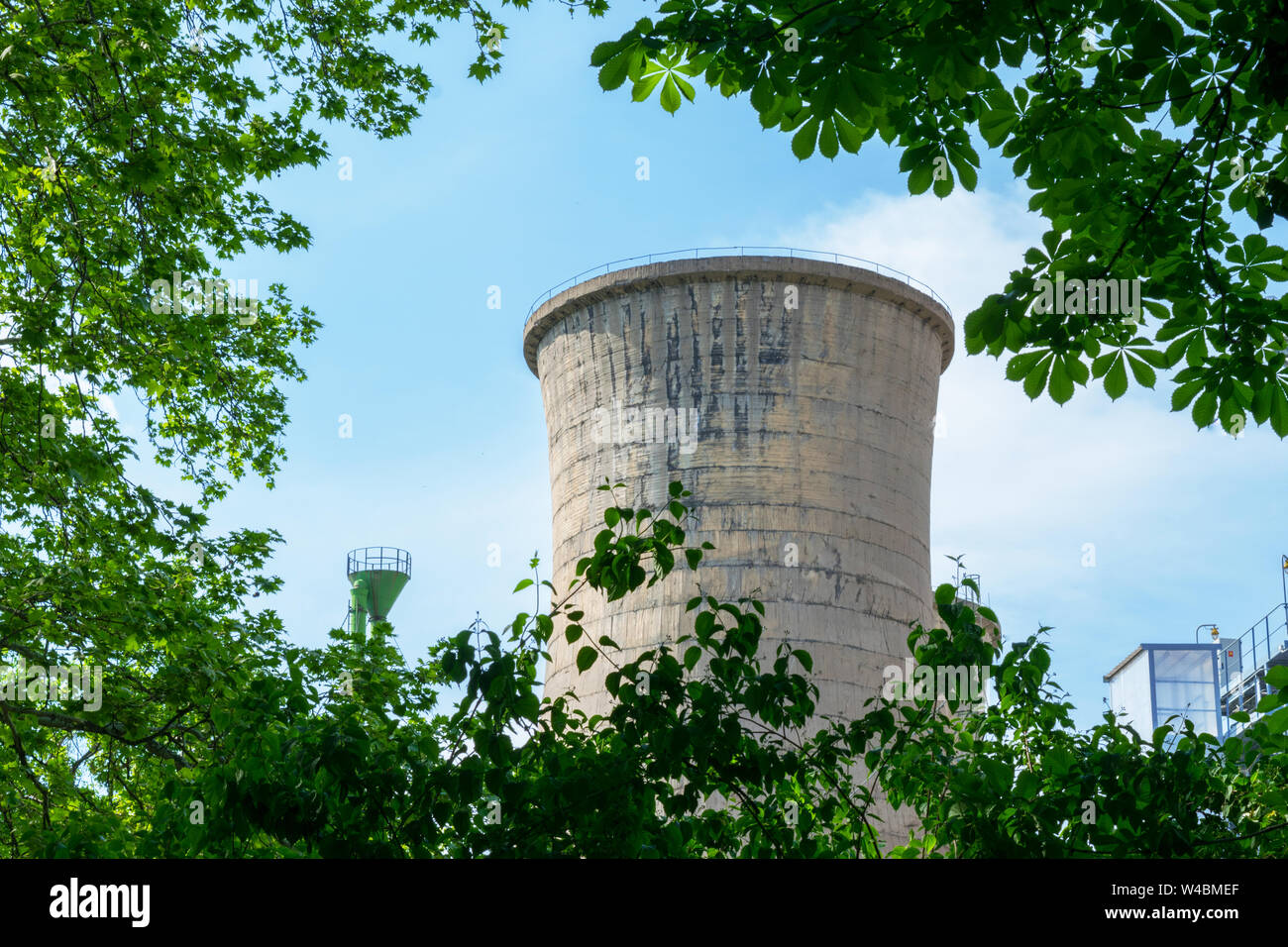 La tour en béton de l'usine d'alimentation cachée parmi la végétation des arbres vert Banque D'Images