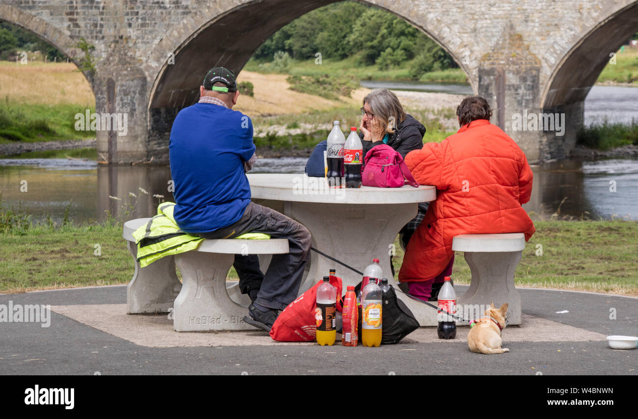 Les gens assis à un banc de pique-nique avec un certain nombre de bouteilles de boisson gazeuse, England, UK Banque D'Images