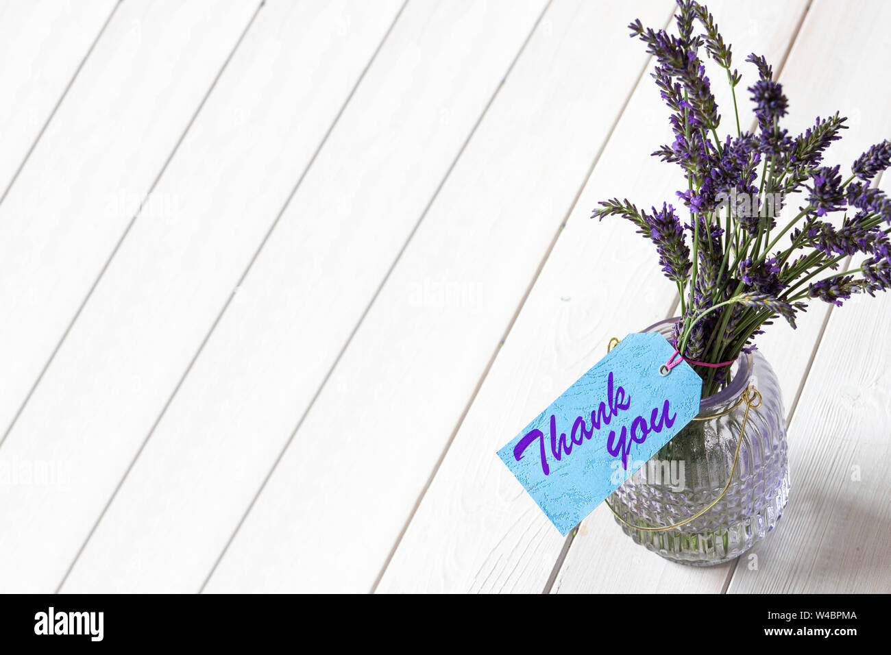 Bouquet de lavande dans un bocal de verre, avec merci écrit sur une étiquette cadeau bleu. Fond de bois blanc Banque D'Images