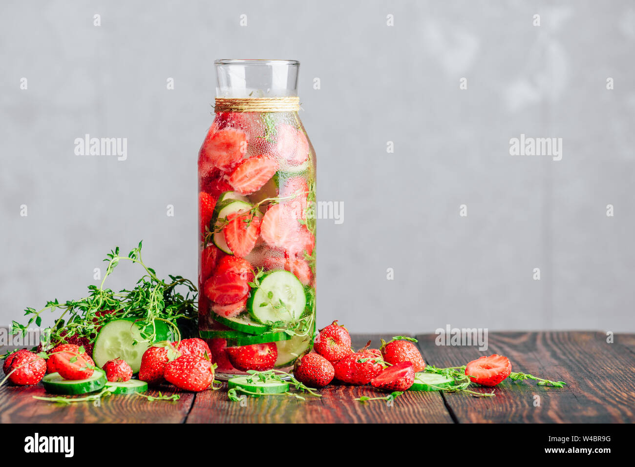Bouteille de l'eau infusée avec des fraises fraîches, tranches de concombre et les ressorts de thym. Ingrédients éparpillés sur une table en bois. Copier l'espace. Banque D'Images