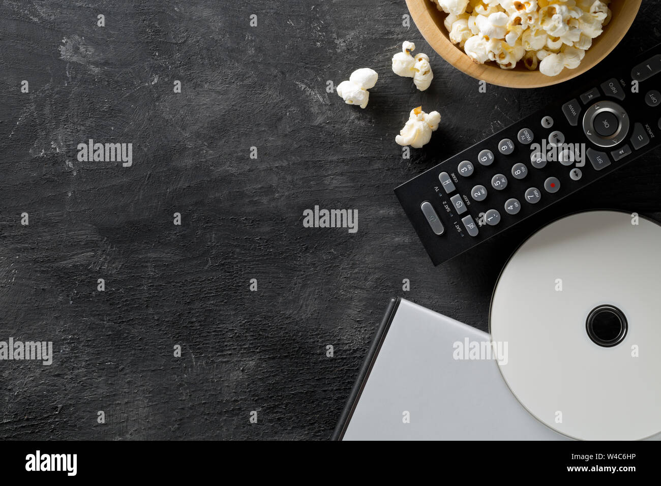DVD ou Blu ray Disc avec la télécommande du téléviseur et le bol de popcorn sur fond sombre. Cinéma maison Cinéma ou séries nuit concept. Vue supérieure mise à plat Banque D'Images