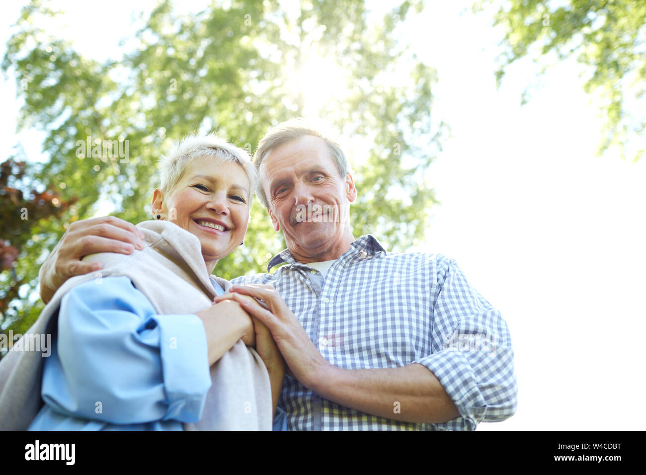 Low angle portrait of happy senior couple looking at camera vers le bas et souriant tout en marchant en parc d'été, copy space Banque D'Images