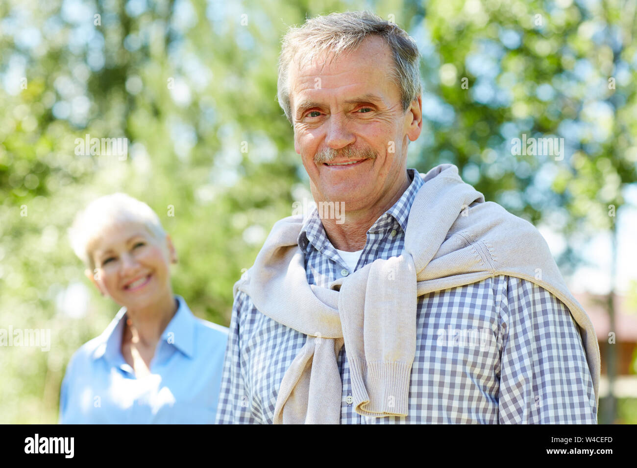 Portrait of senior man contemporain smiling at camera avec femme en arrière-plan, copy space Banque D'Images