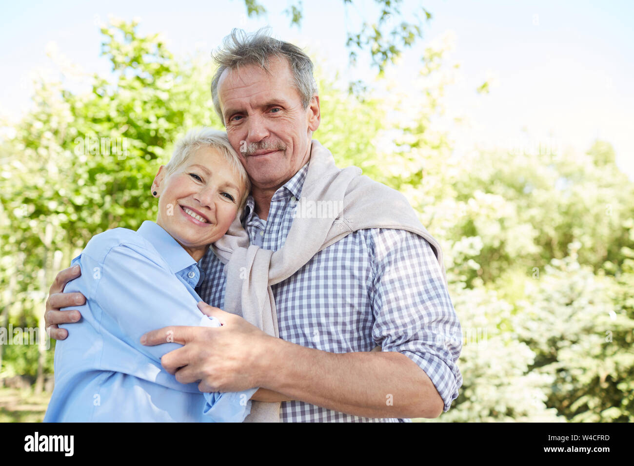 Taille portrait de senior couple embracing and looking at camera tout en profitant de promenade en forêt, copy space Banque D'Images