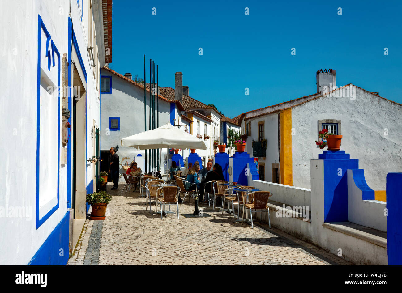 Scène de rue, restaurant en plein air, tables, chaises, vieilles bâtisses blanches, garniture bleu vif, pavés, Europe, Obidos, Portugal, printemps, horizontal Banque D'Images