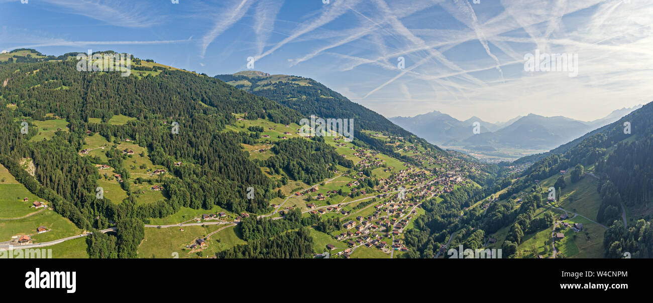 Les images aériennes sur une vallée alpine et les forêts de pins avec chalets et les hautes montagnes qui entourent la vallée. Banque D'Images