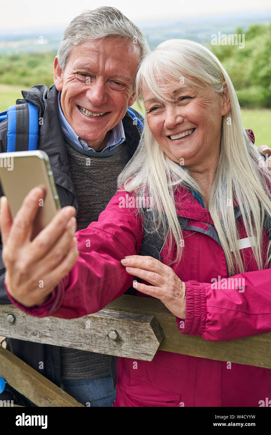 Happy Senior Couple Hiking in Countryside debout près de la porte et en tenant le téléphone mobile Selfies Banque D'Images