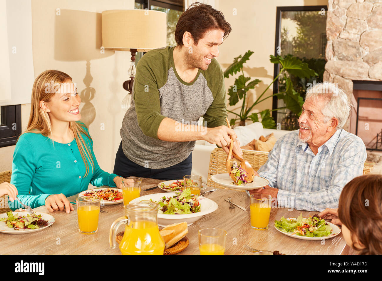 Famille heureuse avec son grand-père en train de dîner ou déjeuner à l'intérieur Banque D'Images