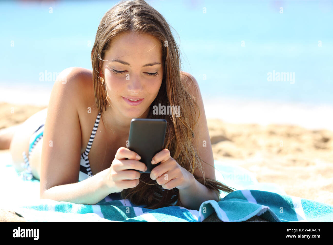 Girl in bikini détendue de soleil allongé sur une serviette à l'aide de smart phone sur la plage en vacances Banque D'Images