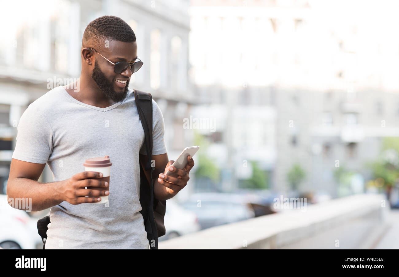 Cheerful homme africain en utilisant son smartphone et de boire du café Banque D'Images