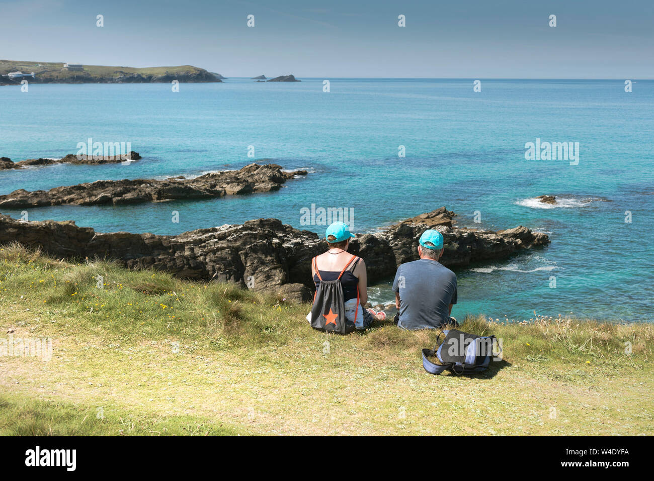 Un couple de vacanciers portant des casquettes de baseball Bleu assis sur la côte donnant sur la mer à Newquay en Cornouailles. Banque D'Images