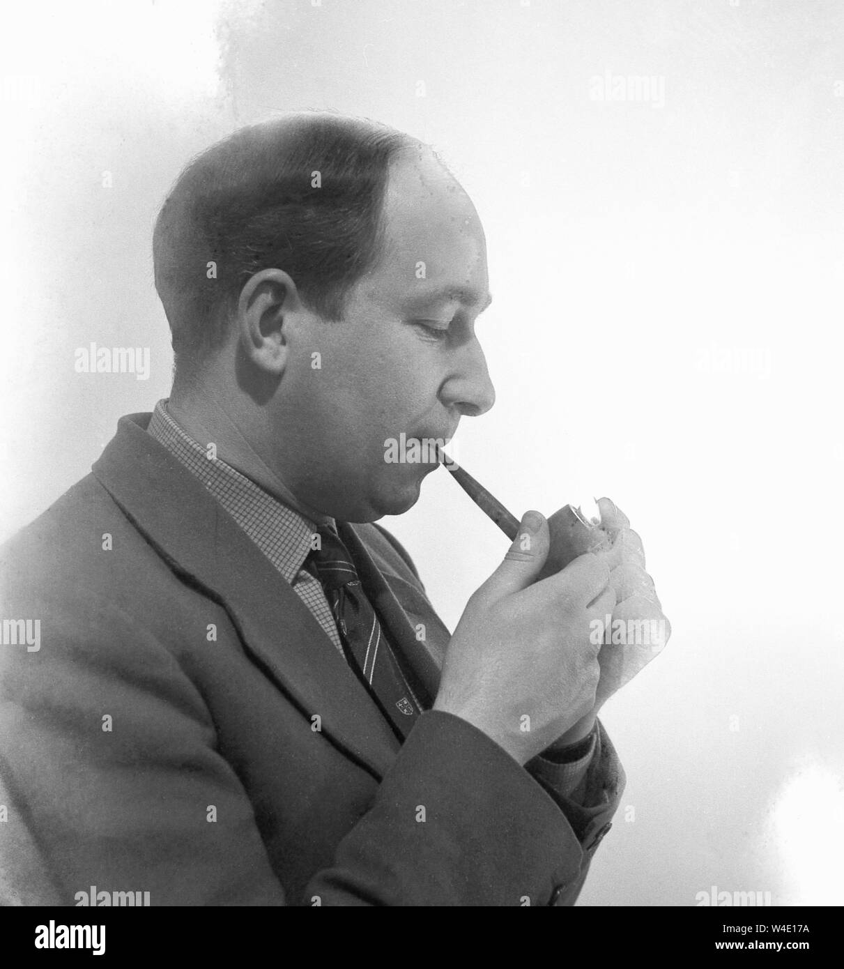 Années 1950, historique, un homme portant une veste et cravate fumer une pipe allumée seulement, avec une flamme, montrant Banque D'Images