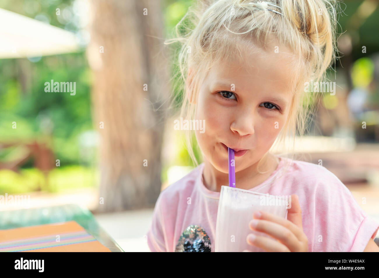 Adorable petit préchooler blanc caucasien blond fille portrait sirotant de délicieux fraisiers en crème au café à l'extérieur. Enfants régime sain et Banque D'Images