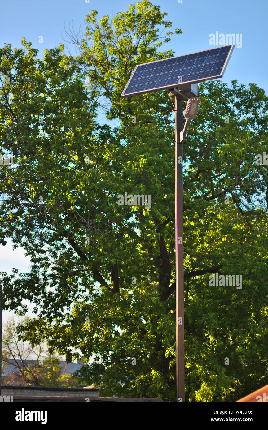 Lampe de rue avec une batterie solaire contre un ciel bleu et arbres Banque D'Images