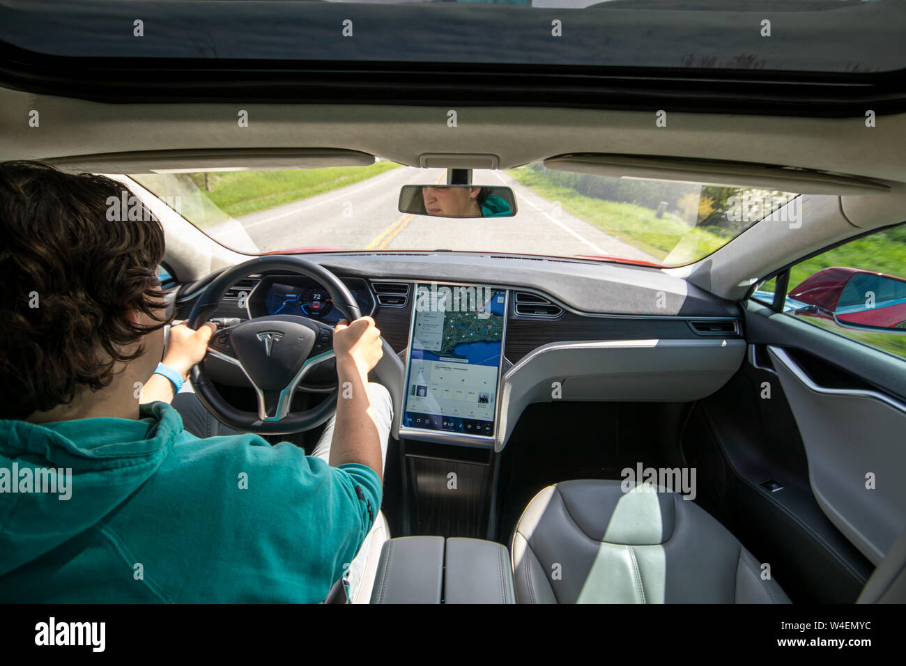 Vue complète de l'homme conduisant Tesla Model S rouge avec la navigation à l'écran à côté. L'intérieur recouvert de cuir noir et gris. Banque D'Images