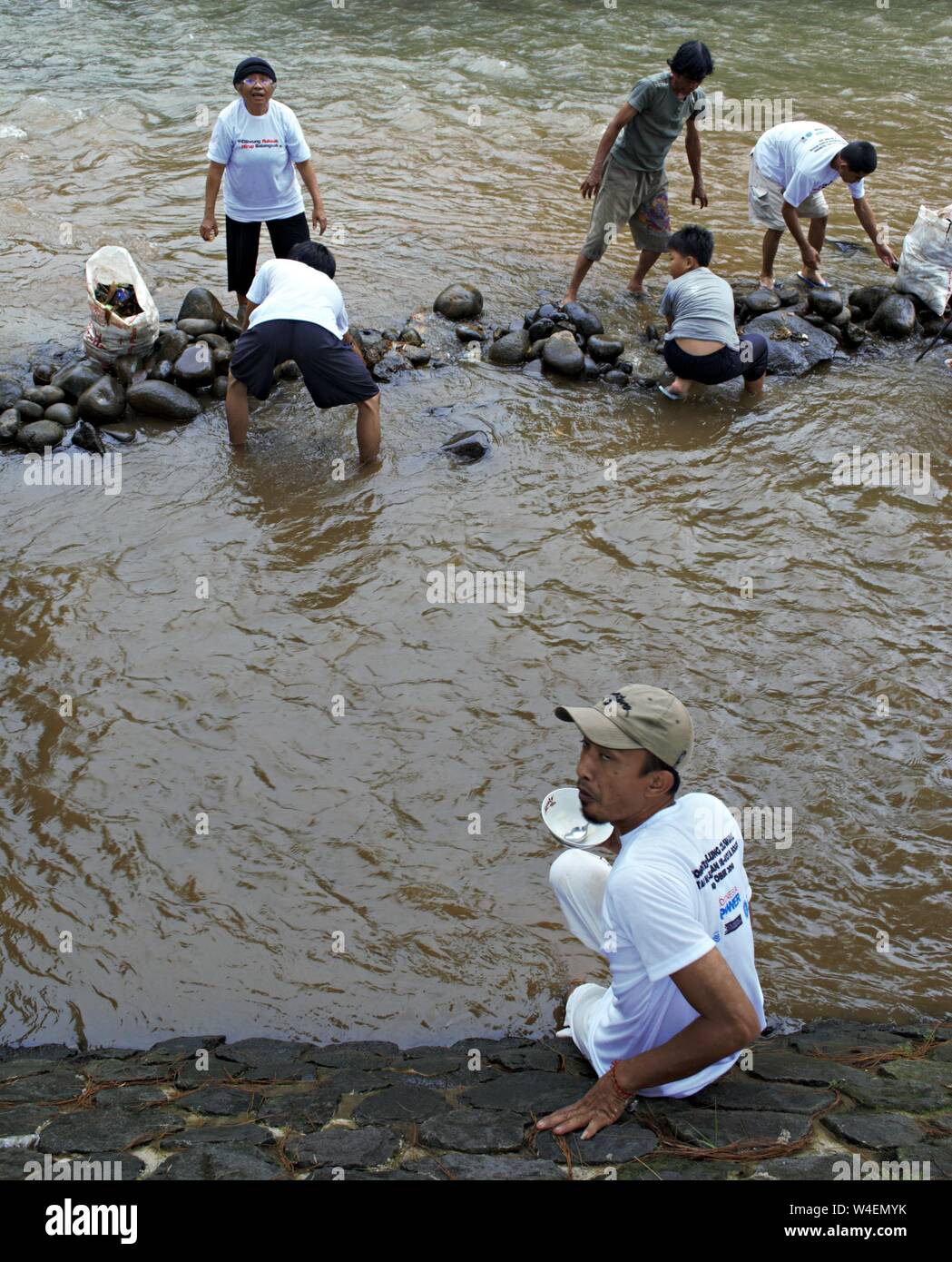 Bogor, Java ouest, Indonésie - Juillet 2019 : un groupe de personnes organiser des pierres pour construire un barrage dans la rivière Ciliwung, alors qu'un homme est assis sur le côté de la rivière. Banque D'Images